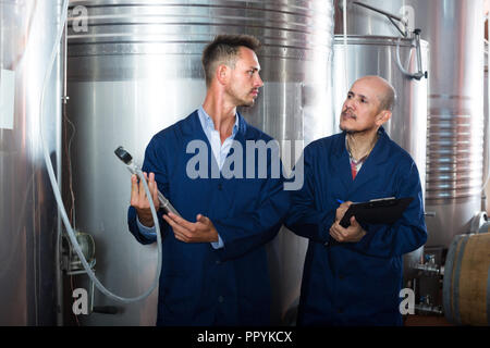 Two winery workers  in uniform working and taking notes in secondary fermentation section Stock Photo
