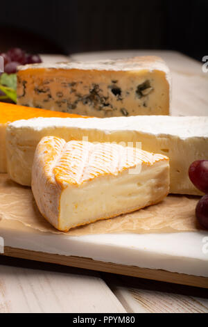 Tasting plate with four France cheeses, cream brie, marcaire, saint paulin and blue auvergne cheese, served with fresh ripe grapes close up Stock Photo