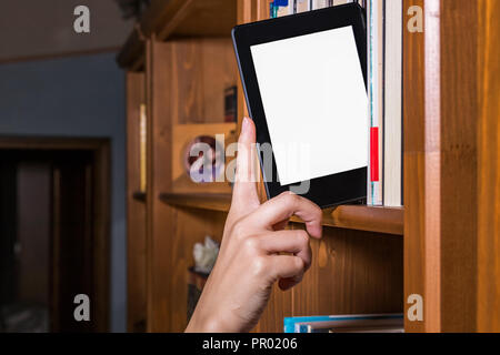 Woman hand choosing e reader among books on a bookshelf Stock Photo