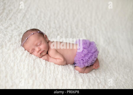 Portrait of a sleeping, 2 week old newborn baby girl wearing frilly, lavender purple bloomers and a pearl headban. Shot in the studio on a white blank Stock Photo