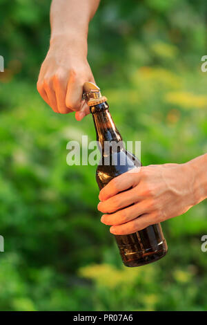 Young man is opening bottle of beer with old opener on natural blurred background Stock Photo