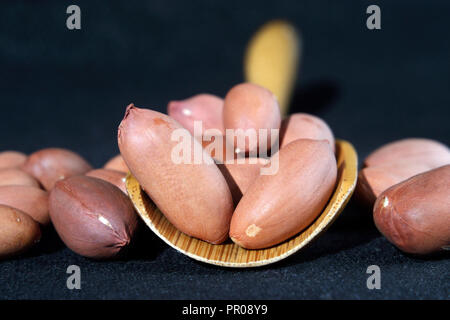 Peeled peanuts with wooden spoon on dark background Shallow depth of field Stock Photo