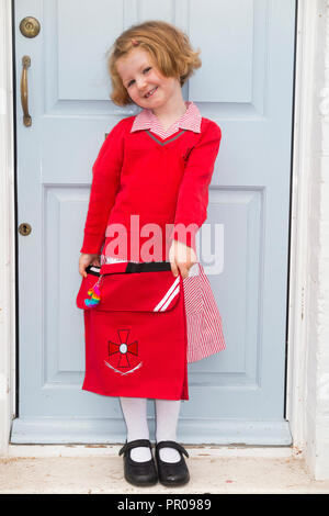 Four year old schoolgirl / school girl / child / kid in new uniform at her front door, leaving home for school on her 1st / first day of school. UK. Stock Photo