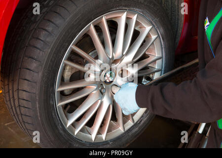 Tyre fitter / mechanic tightens / tightening / checking the nuts with a wrench on a car wheel that's just been fitted with a new tyre / tire. UK (102) Stock Photo