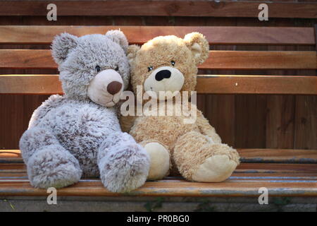 Two teddy bears sitting on a bench in a garden. Stock Photo