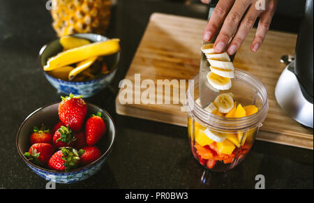 Hands of woman putting fruits in grinder bowl. Female making mix fruit smoothie in kitchen. Stock Photo