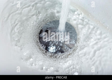 Closeup of tap water flowing into stainless steel drain of white washbasin background Stock Photo