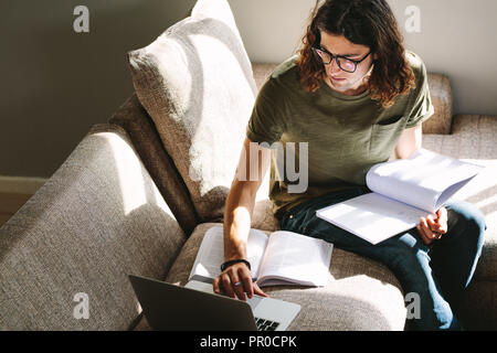 Male student looking at a laptop while studying. Student preparing for college exams sitting at home. Stock Photo