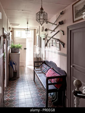 Tapestry cushions on vintage bench in tile hallway with swords and muskets Stock Photo