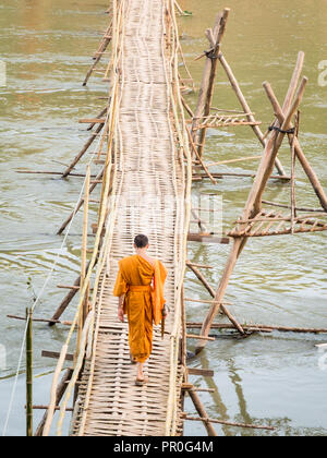 Orange-clad Buddhist monk crossing a bamboo bridge, Luang Prabang, Laos, Indochina, Southeast Asia, Asia Stock Photo