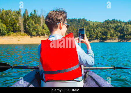 Young woman taking selfie with smart phone while kayaking on the Lokvarsko lake in Gorski kotar, Croatia. Girl enjoying adventurous experience on Stock Photo