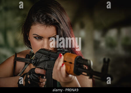 Attractive girl standing in the attitude of aiming and looking through the sight automatic rifle. Stock Photo