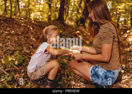 Beautiful young mother and her daughter in the forest looking at the map to find direction. Stock Photo