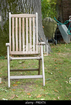 Iroko wooden chair in front of an oak tree in an english garden at the onset of autumn Stock Photo
