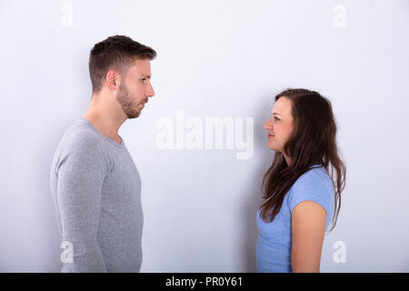 Two Businesspeople Looking At Each Other In Front Of Grey Background Stock Photo