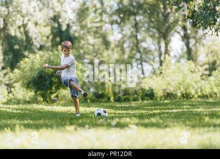 full length view of happy boy playing with soccer ball on grass in park Stock Photo