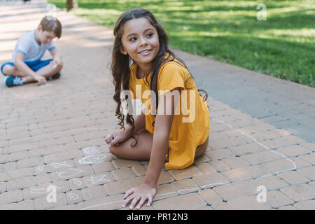 Cute boy and girl drawing with chalk on the sidewalk in the park ...