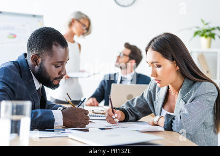 side view of young multicultural businesspeople writing something in office Stock Photo