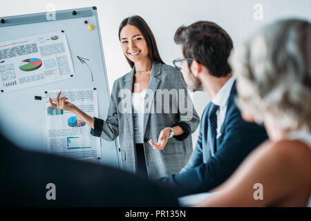 smiling asian businesswoman pointing on flipchart during meeting in office Stock Photo