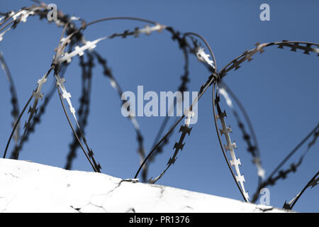Barbed wire on top of white wall under blue sky background, close-up photo with selective focus Stock Photo