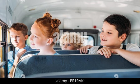 group of schoolchildren riding on school bus and looking through window Stock Photo