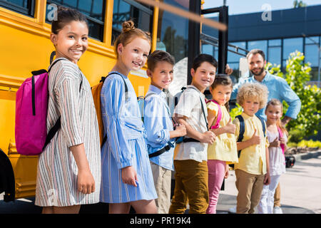 queue of pupils standing near school bus with teacher Stock Photo - Alamy