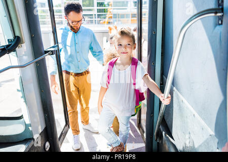 schoolgirl entering school bus with teacher while going on excursion Stock Photo