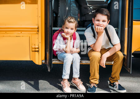 adorable little scholars sitting on stairs of school bus Stock Photo