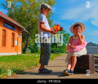 Adorable little girl and boy on a railway station, waiting for the train with vintage suitcase. Traveling, holiday and chilhood concept. Travel insura Stock Photo