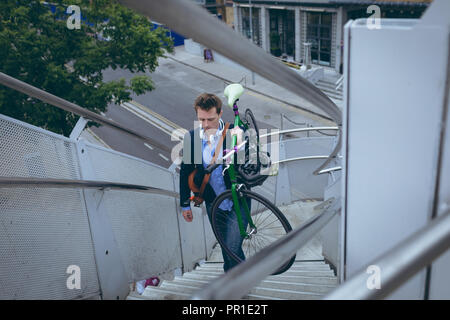 Businessman walking up stairs with bicycle Stock Photo