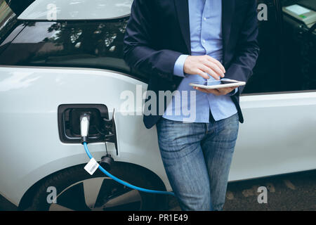 Businessman using digital tablet while charging electric car Stock Photo