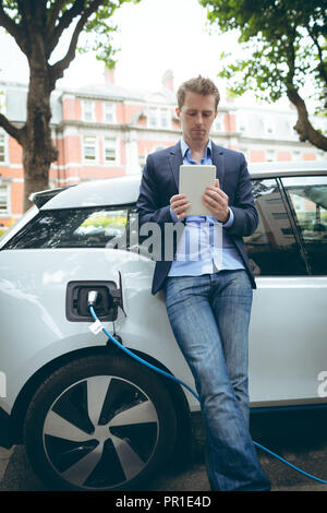 Businessman using digital tablet while charging electric car Stock Photo