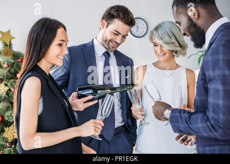 happy businessman pouring champagne to multicultural colleagues glasses in office Stock Photo