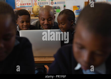 Male teacher using laptop with students in the classroom Stock Photo