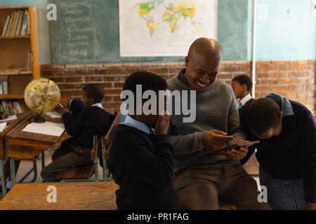 Male teacher using digital tablet with students in classroom Stock Photo