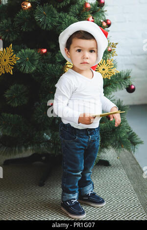 cute boy in santa hat holding star while decorating christmas tree Stock Photo