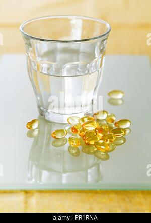 Evening primrose oil capsules in a pile next to a glass of water. Stock Photo