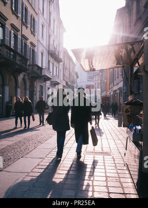 Two shadow lady figures giving their back walking away after shopping in the sunset. A small stand is to be seen on the right. Other people walk. Stock Photo