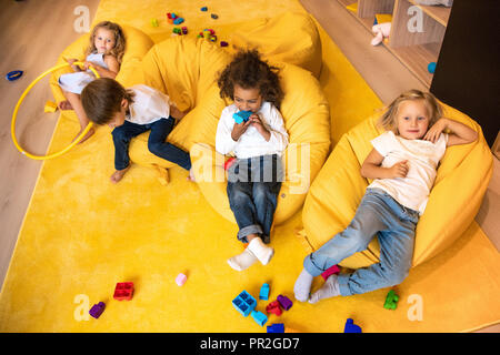 high angle view of multicultural kids lying on bean bag chairs in kindergarten Stock Photo
