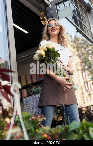 low angle view of beautiful happy florist going out from flower shop with roses in jar Stock Photo