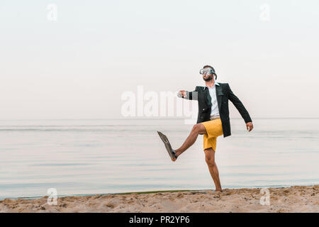 man in black jacket and shorts walking with swimming mask and flippers on sandy beach Stock Photo