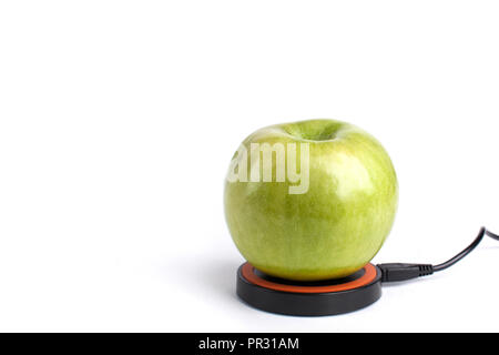 Green apple lies on a platform for wireless charging on an isolated white background Stock Photo