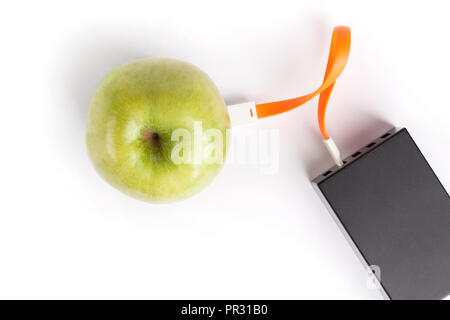 Green apple connected by an orange cable to a charger on a white isolated background Stock Photo