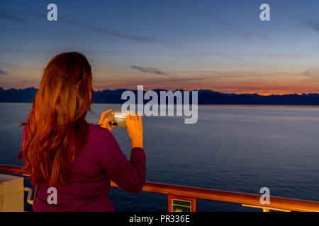 Juneau, Alaska, USA - Aug 20, 2018. Girl taking sunset picture from Alaska cruise ship Stock Photo