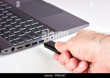 Hand of a man plugging a black USB Flash drive into a silver laptop port with a black keyboard. On a white background. Stock Photo