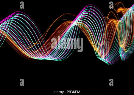 Long exposure light painting photography, curvy lines of vibrant neon pink , green parallel lines and metallic yellow gold against a black background Stock Photo