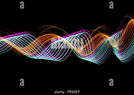 Long exposure light painting photography, curvy lines of vibrant neon pink , green parallel lines and metallic yellow gold against a black background Stock Photo