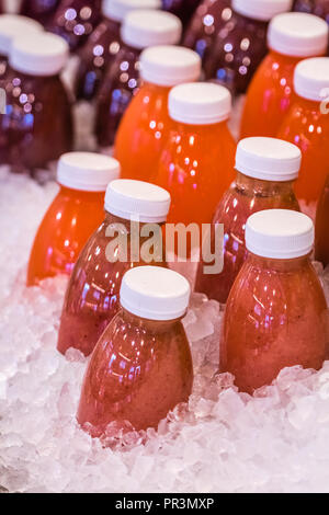 Freshly prepared organic fruit smoothies stored in plastic bottles in ice on a display on a food stall in a market Stock Photo