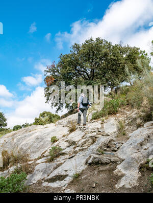 Older man wearing backpack walking on rocky hillside of GR 249 mountain walking route, Sierras de Tejeda Natural Park, Axarquia, Andalusia, Spain Stock Photo