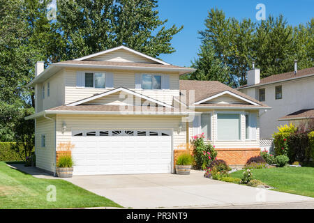 A perfect neighbourhood. Family house with landscaped front yard and concrete driveway on sunny day in British Columbia Stock Photo